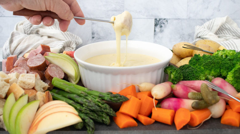 Hand pulling dipper out of cheese fondue bowl