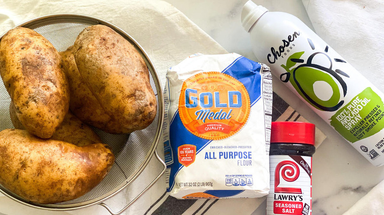 Ingredients for baked jojos including potatoes in bowl, flour and oil