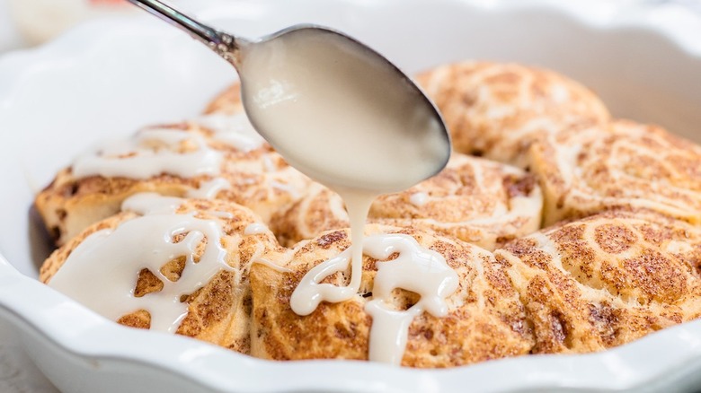 spoon drizzling icing onto rolls