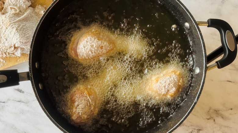 Chicken drumsticks frying in pot of oil