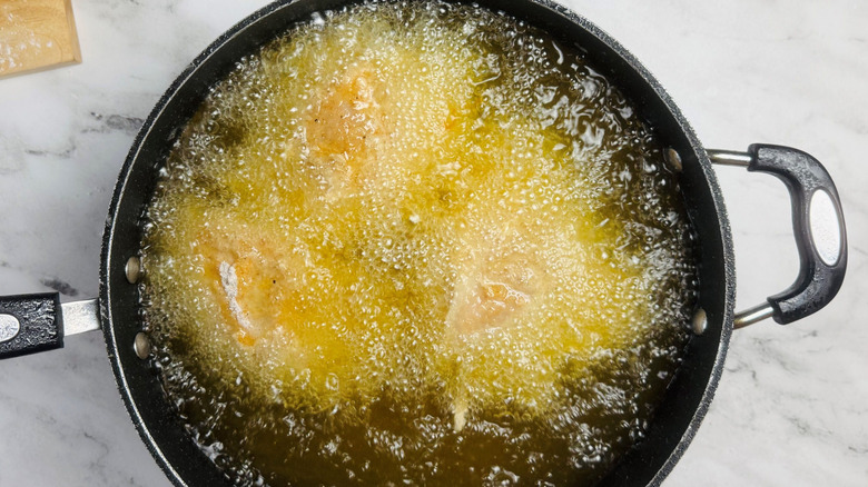 Chicken frying in pot of oil