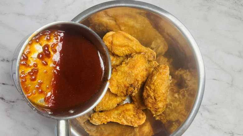 Saucepan of BBQ sauce pouring onto fried chicken