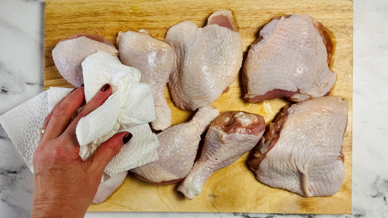 Hand using paper towels to pat raw chicken on wooden board