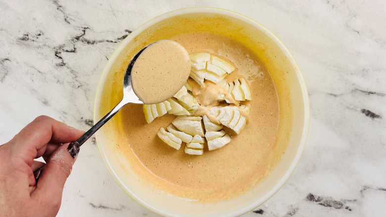 Hand spooning batter over onion in bowl