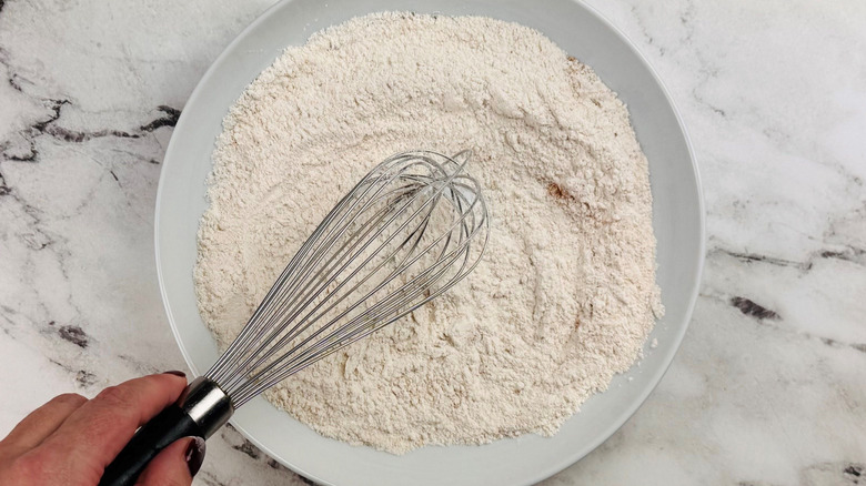 Hand whisking seasoned flour mixture on plate