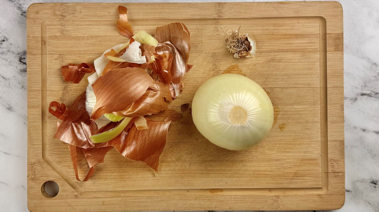 Peeled onion and pile of onion skin on cutting board