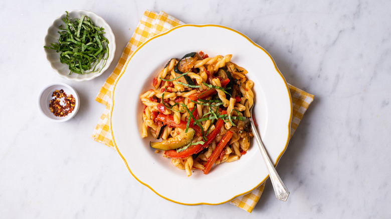 Summer vegetable pasta in a white bowl next to basil and chili flakes.