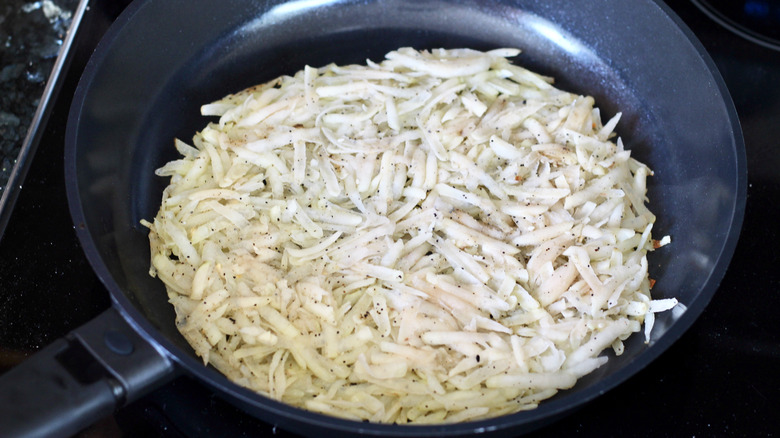 Shredded potatoes added to black pan