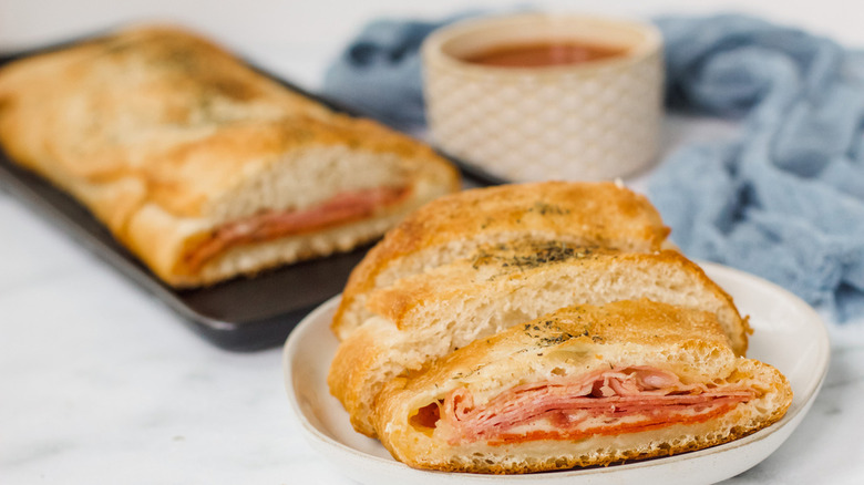 stromboli on a white plate with a container of dipping sauce  and a baking tin of stromboli nearby