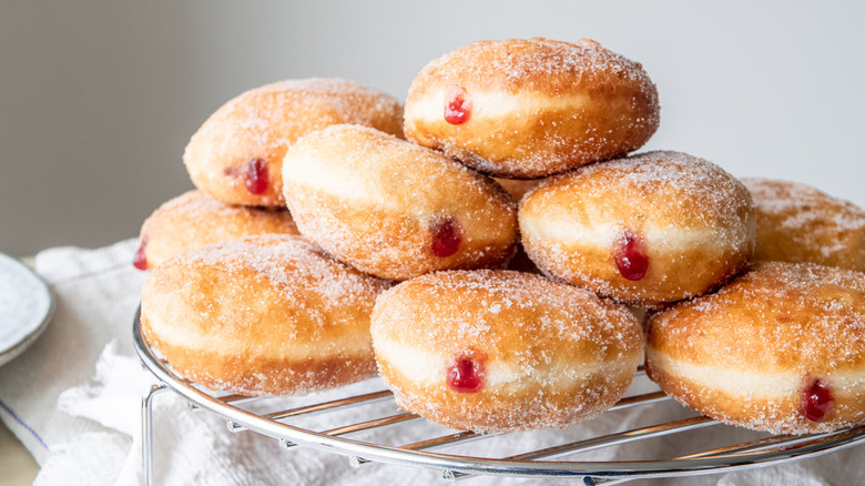 silver wire cooling rack of donuts covered in granulated sugar and filled with seedless raspberry jam