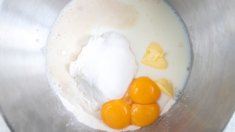 metal mixing bowl with three egg yolks, butter, flour, warm milk, sugar, salt, and yeast