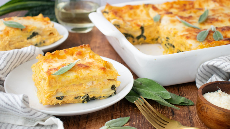 Slice of pumpkin lasagna on plate with lasagna in casserole dish in background