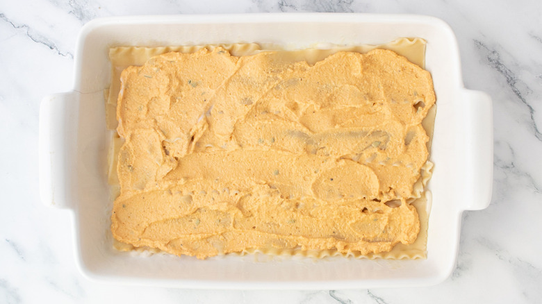 Lasagna noodles topped with pumpkin ricotta in casserole dish