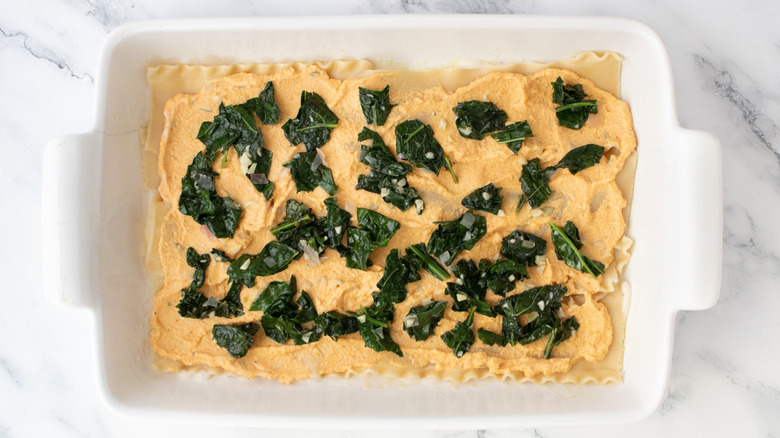 Lasagna noodles topped with pumpkin ricotta and sauteed kale in casserole dish