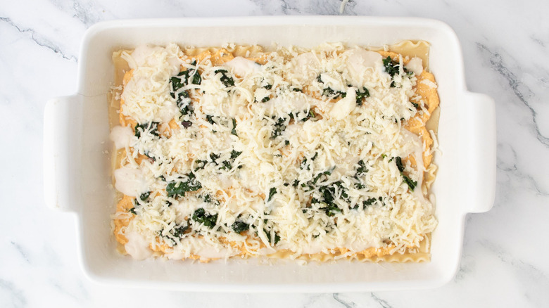 Pumpkin lasagna layer with noodles, Alfredo sauce, kale, and cheese in casserole dish