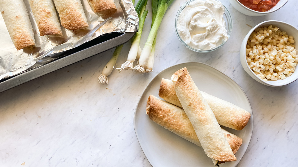 taquitos on baking sheet and on a white plate