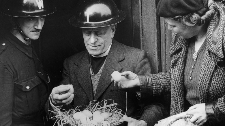 black and white photo of woman holding an egg next to two men in helmets