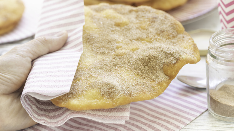 Hand holds elephant ear with cinnamon sugar in striped napkin