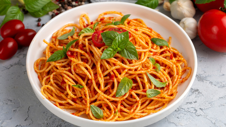 A bowl of spaghetti with tomato sauce next to fresh tomatoes, garlic, and basil