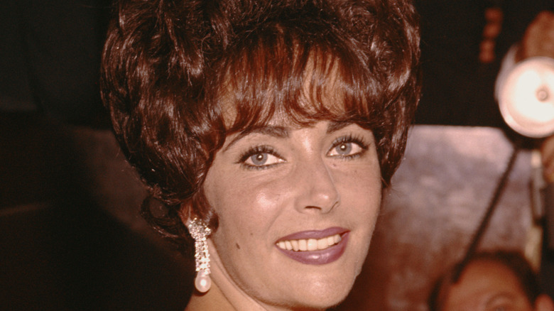 Hollywood star Elizabeth Taylor smiling at the camera with bejeweled earrings