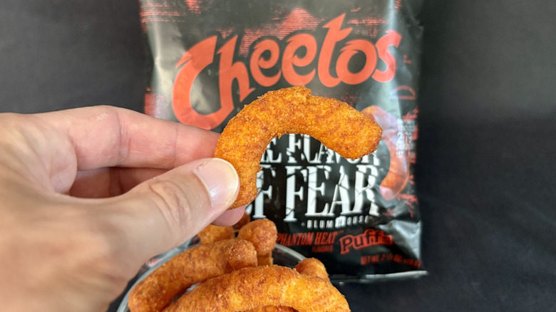 Hand holding a Cheetos puff in front of the bag