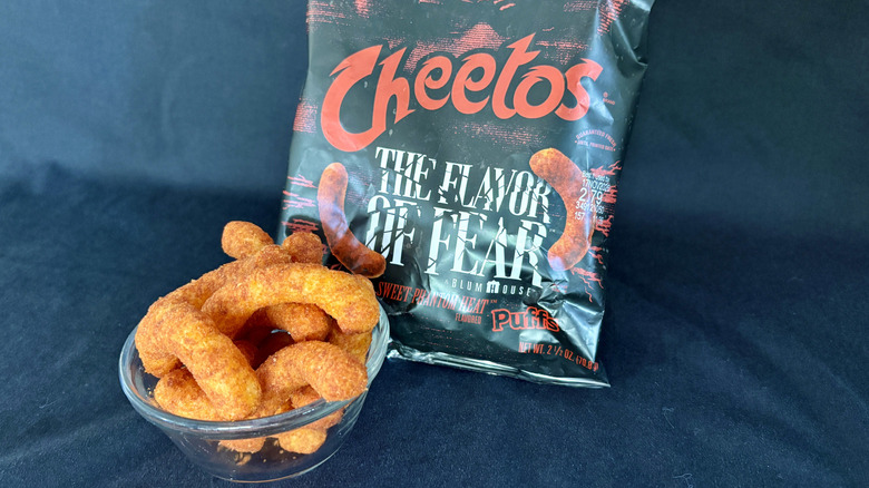 A glass bowl holding Cheetos in front of a black Cheetos bag