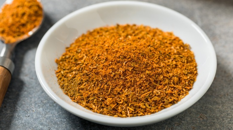 Small white bowl of Cajun seasoning with metal spoon.