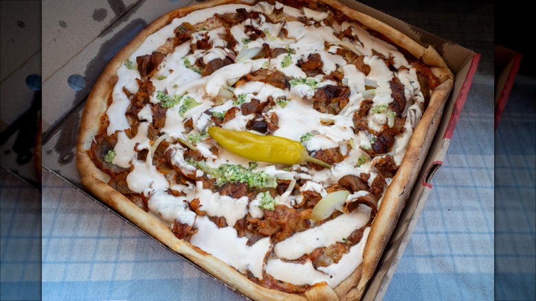 A doner kebab pizza in box with a hot pepper.