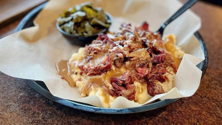 Mashed potatoes with brisket, gravy, and side of collard greens on paper-lined tray.