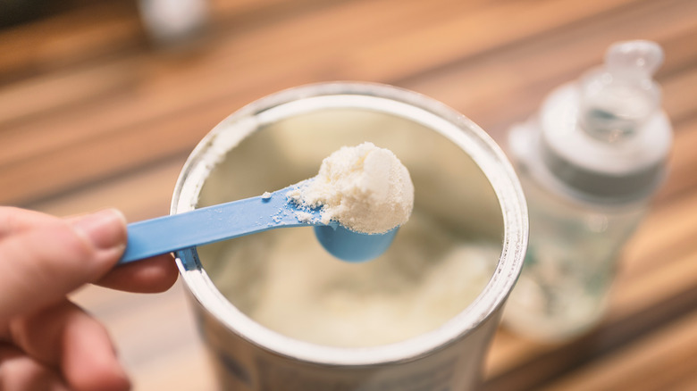 Person scooping baby formula with blue spoon