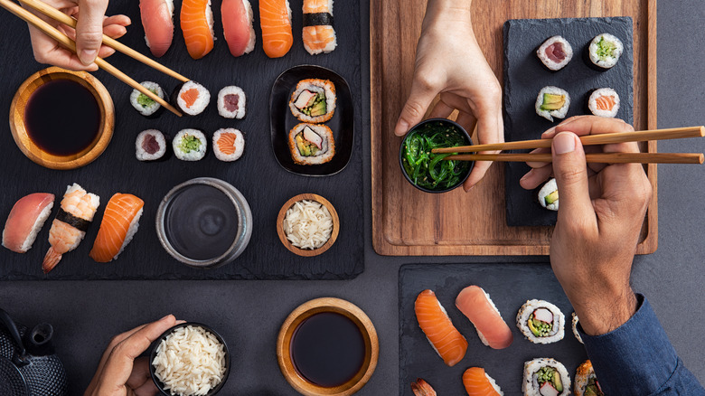 Hands with chopsticks reaching for sushi