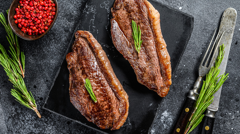 Grilled sirloin steaks on marble board next to leaf sprigs