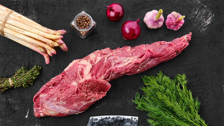 Whole tenderloin alongside various ingredients on black surface