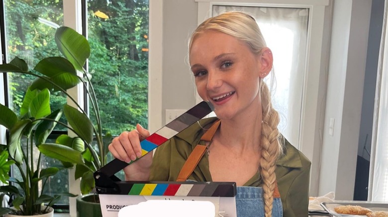 Tineke Younger smiles while holding up a slate on set
