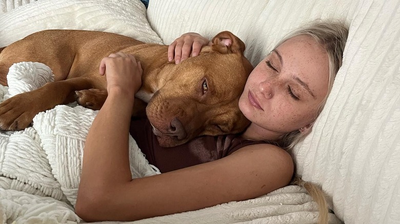 Tineke Younger lies down holding a dog in her arms