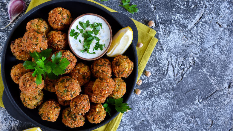 Falafel balls on a plate with lemon, sauce, and herbs