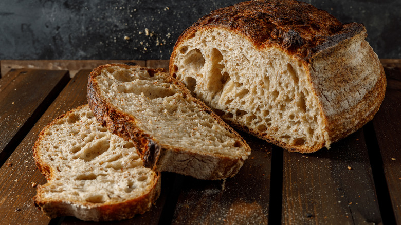 A sourdough loaf on wooden table with two slices cut