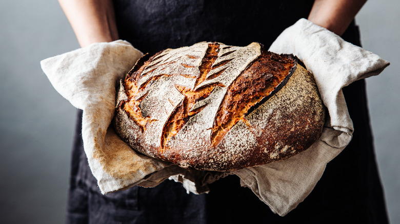 Hands holding home baked sourdough loaf in linen towel