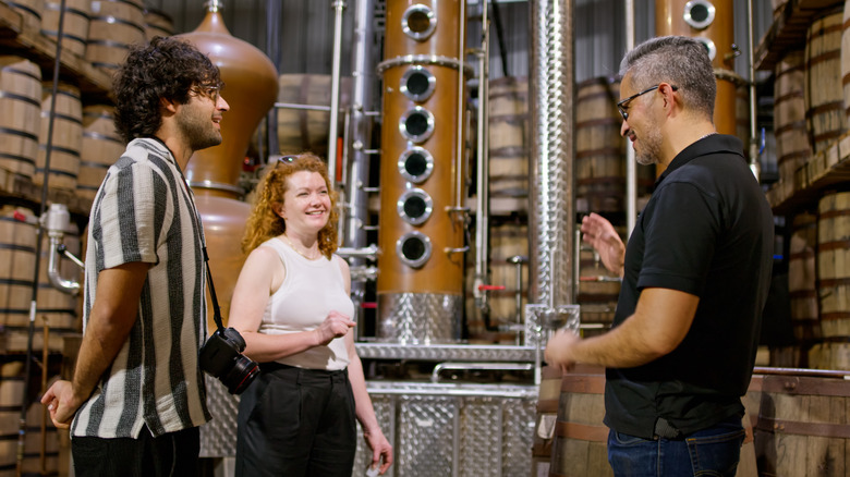 Two people on a distillery tour with barrels in background