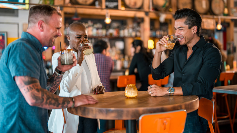 Three friends sitting around a table laughing and drinking