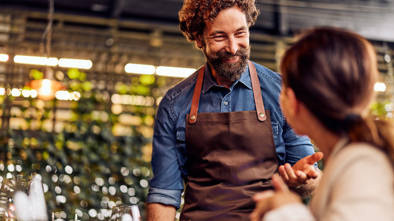 Blurred customer in foreground speaking with smiling bartender