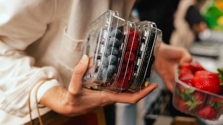 Person holding several packs of berries in grocery store