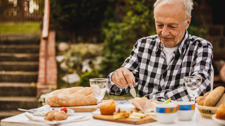 Older man sitting in a garden enjoying cheese and bread at a table