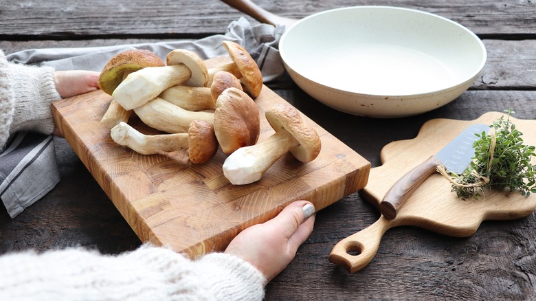 hands holding mushrooms on a cutting board in kitchen