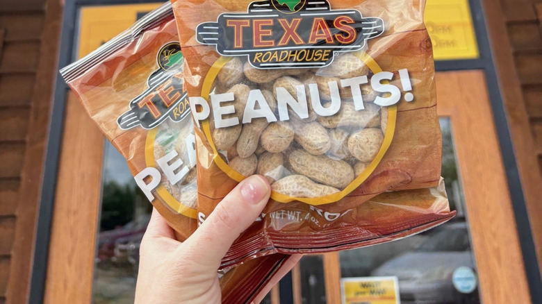 Hand holding two bags of branded Texas Roadhouse peanuts