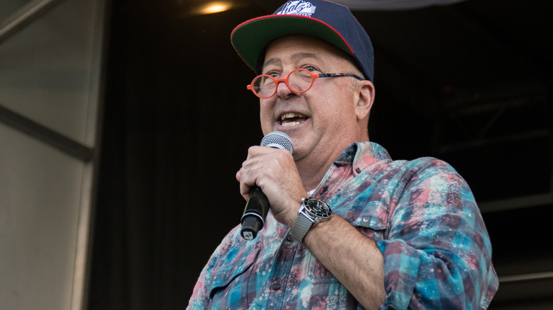 Andrew Zimmern wearing hat and holding microphone