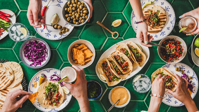 Hands grabbing tacos, sides and tequila drinks