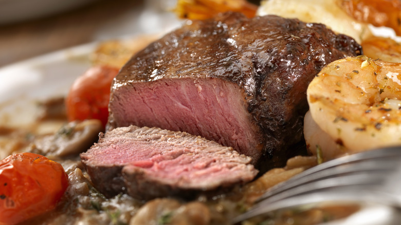 cutting into steak, shrimp and vegetables