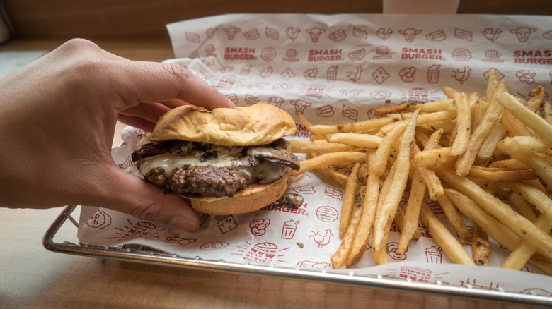 hand holding Smashburger next to fries