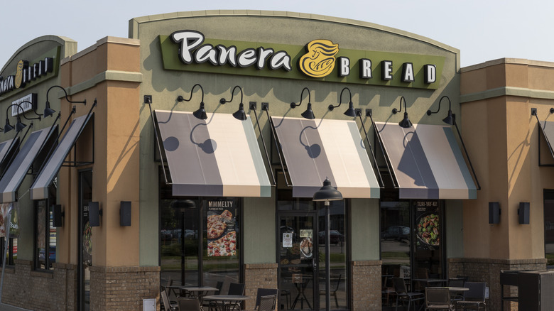 Exterior of Panera Bread, with product advertisements in windows and outdoor seating.